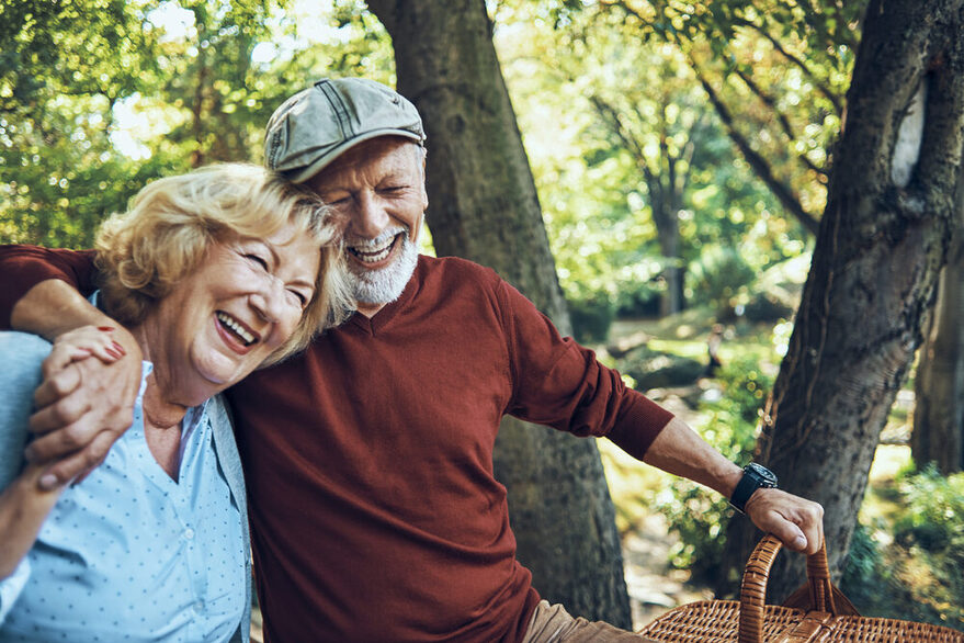 Ein fröhliches Ehepaar fortgeschrittenen Alters lacht, während sie einen Ausflug in den Wald zu machen scheinen.
