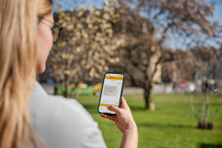 Eine Frau schaut im Schlossgarten in ihr Smartphone, wo der Chatbot der Stadt Stuttgart zu sehen ist.