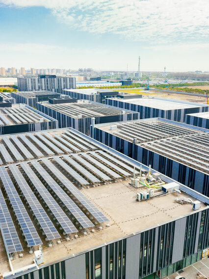 Modern buildings with solar panels on the roof can be seen in the foreground. A town can be seen in the background.
