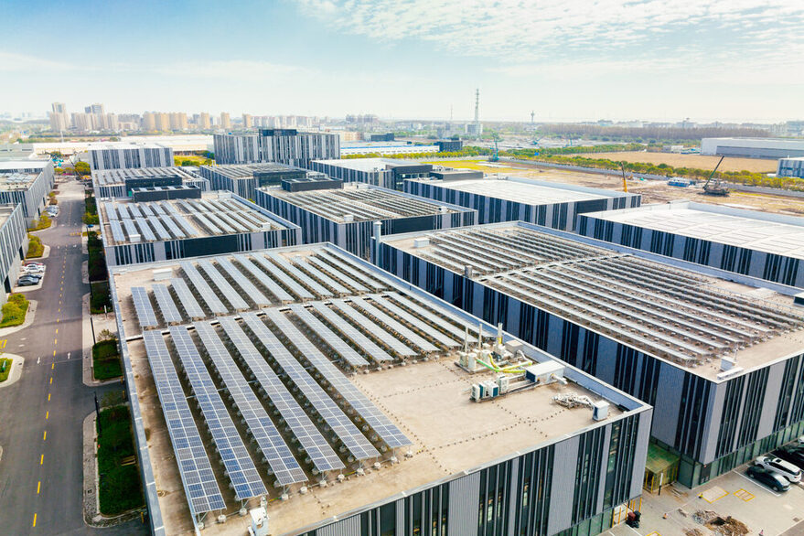 Im Vordergrund sind moderne Gebäude mit Solaranlagen auf dem Dach zu sehen. Im Hintergrund ist eine Stadt zu erkennen.