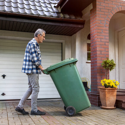 Ein Mann rollt eine grüne Abfalltonne über einen Hof.