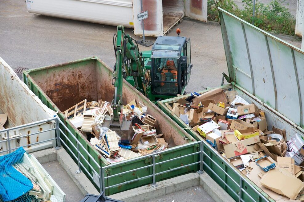 Ein Mitarbeiter der AWS sitzt in einem Bagger und füllt einen Container mit Abfall.