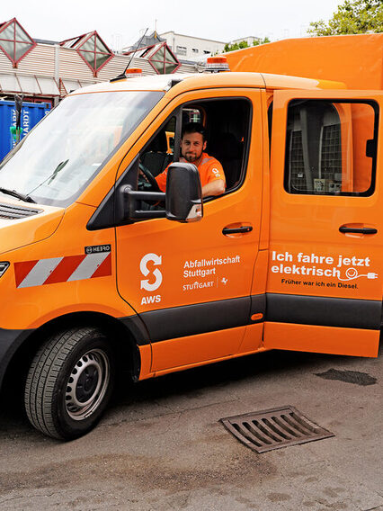 Ein orangenes Fahrzeug der AWS und zwei Mitarbeitende.