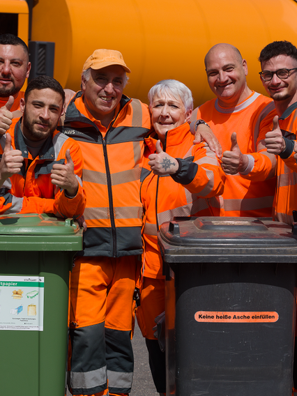 Einige Mitarbeiter der AWS stehen vor einem Müllfahrzeug und lächeln.