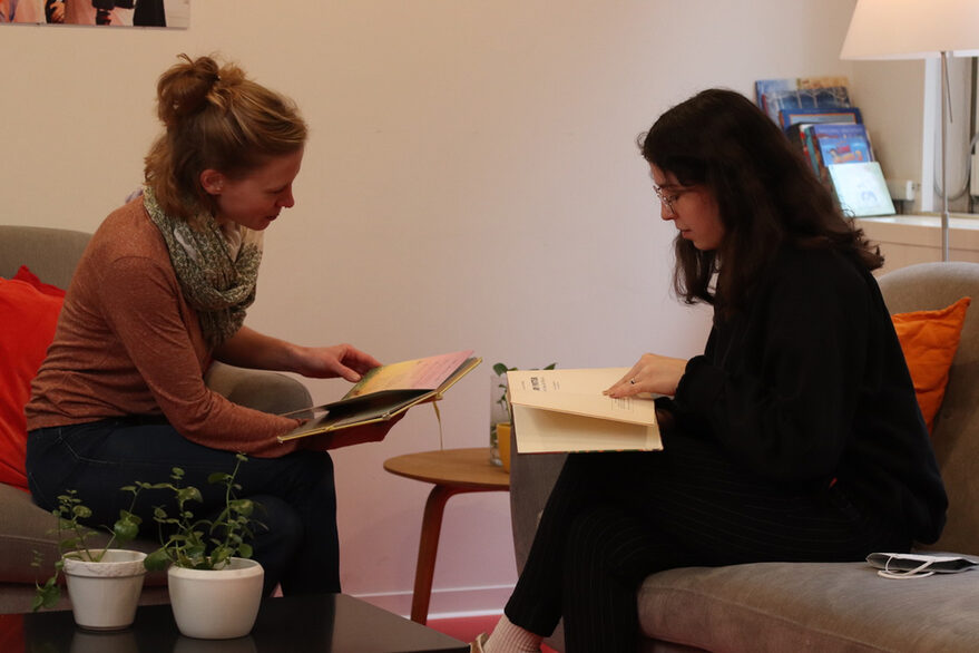 Zwei Frauen, die sich auch zwei Sofas gegenübersitzen und jeweils ein Buch in der Hand halten.