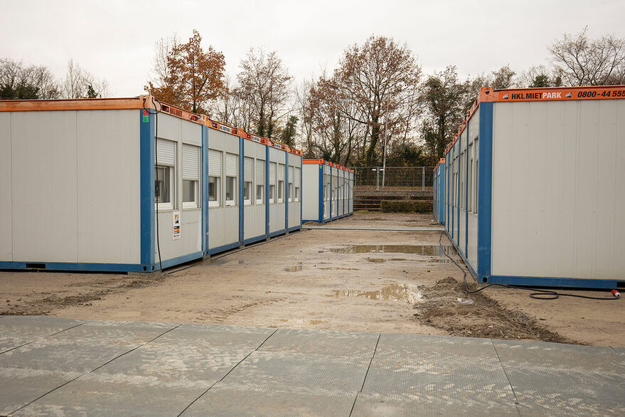 links und rechts je eine Reihe mit grauen Wohncontainern und vorne im Bild ein provisorischer Weg