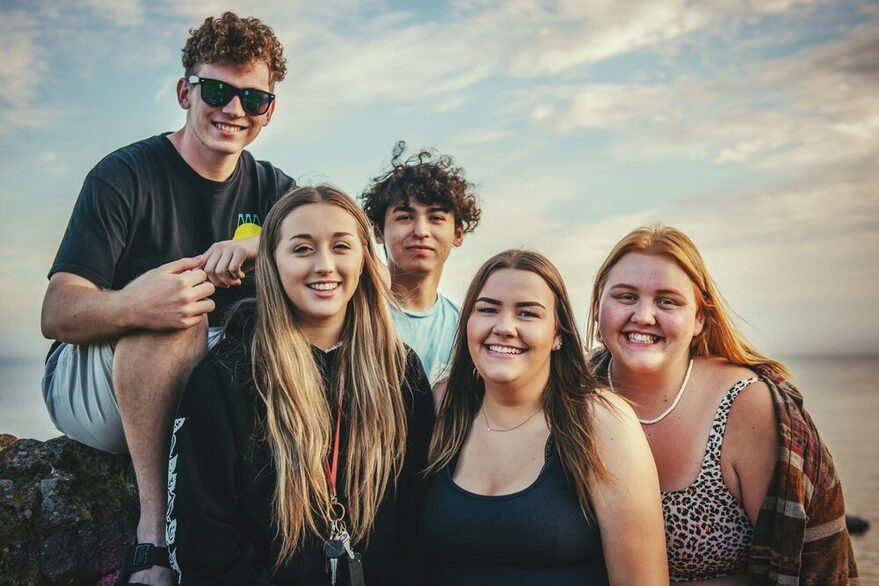 Eine Gruppe Jugendlicher ist vor einem Meerespanorama abgebildet und lächelt in die Kamera.