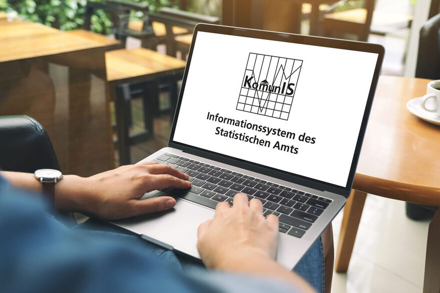 ine Person sitzt vor einem Tisch mit einem Lapot. Auf dem Bildschirm steht die Aufschrift: Informationssystem Komunis des Statistischen Amts.