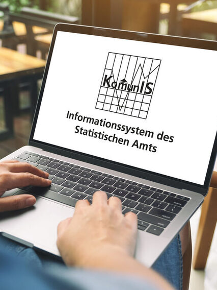 ine Person sitzt vor einem Tisch mit einem Lapot. Auf dem Bildschirm steht die Aufschrift: Informationssystem Komunis des Statistischen Amts.