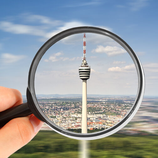 Eine Person hält eine Lupe in der Hand. Im Vergrößerungsglas ist der Fernsehtum Stuttgart zu sehen.