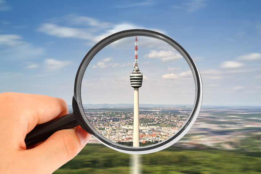 Eine Person hält eine Lupe in der Hand. Im Vergrößerungsglas ist der Fernsehtum Stuttgart zu sehen.