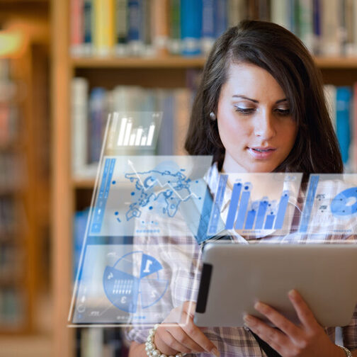 Eine Studentin steht in einer Bibliothek und hält ein Tablet in der Hand.