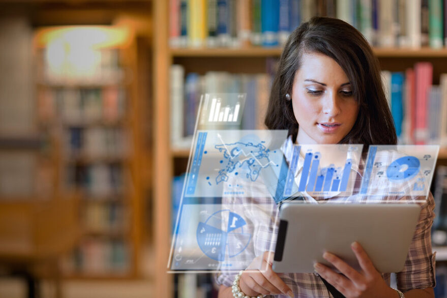 Eine Studentin steht in einer Bibliothek und hält ein Tablet in der Hand.