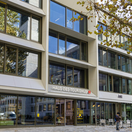 Moderne Außenfassade des Haus des Tourismus am Marktplatz in Stuttgart. In der großen Fensterfront spiegelt sich der Marktplatz mit dem Rathausturm wieder.