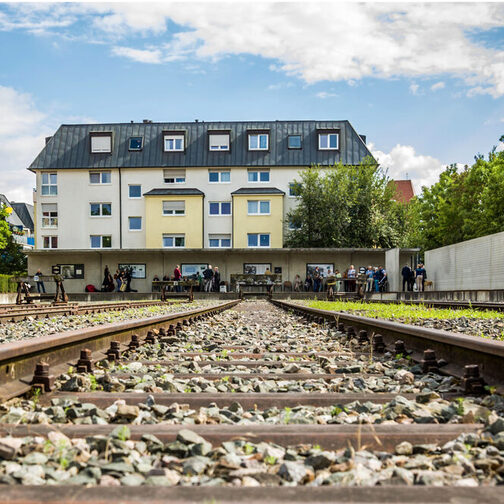 Gedenkfeier Gedenkstätte Nordbahnhof, Gleisverlauf im Hintergrund ist ein Haus