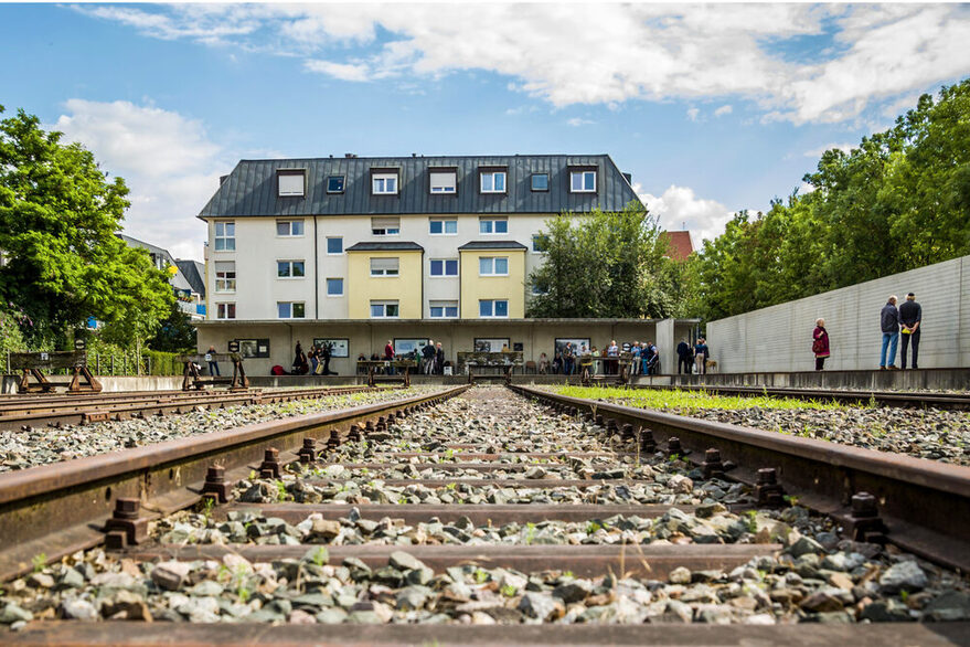 Gedenkfeier Gedenkstätte Nordbahnhof, Gleisverlauf im Hintergrund ist ein Haus