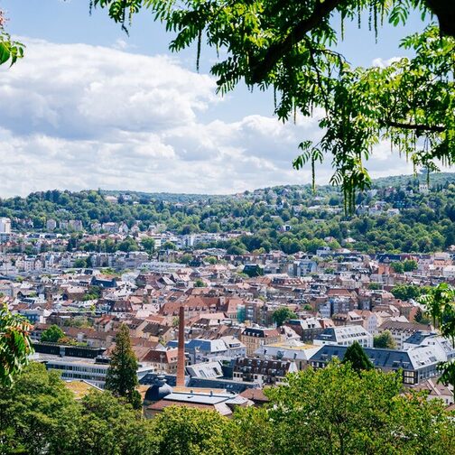 Panoramablick von oben auf Stuttgart mit Häuserdächern und vielen grünen Flächen.