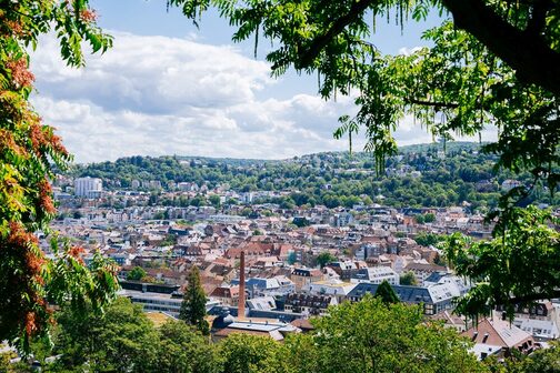 Panoramablick von oben auf Stuttgart mit Häuserdächern und vielen grünen Flächen.