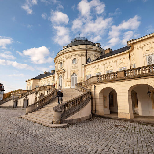 Außenansicht von Schloss Solitude: Zwei Menschen steigen die Freitreppen hinauf.