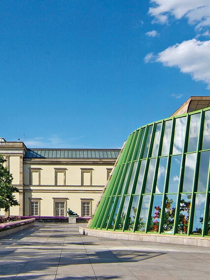 Neue Staatsgalerie mit geschwungener Travertin-Fassade, mit pinken und blauen Handläufen an den Treppen sowie grünen Stahlträgern.