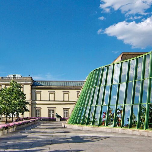 Neue Staatsgalerie mit geschwungener Travertin-Fassade, mit pinken und blauen Handläufen an den Treppen sowie grünen Stahlträgern.