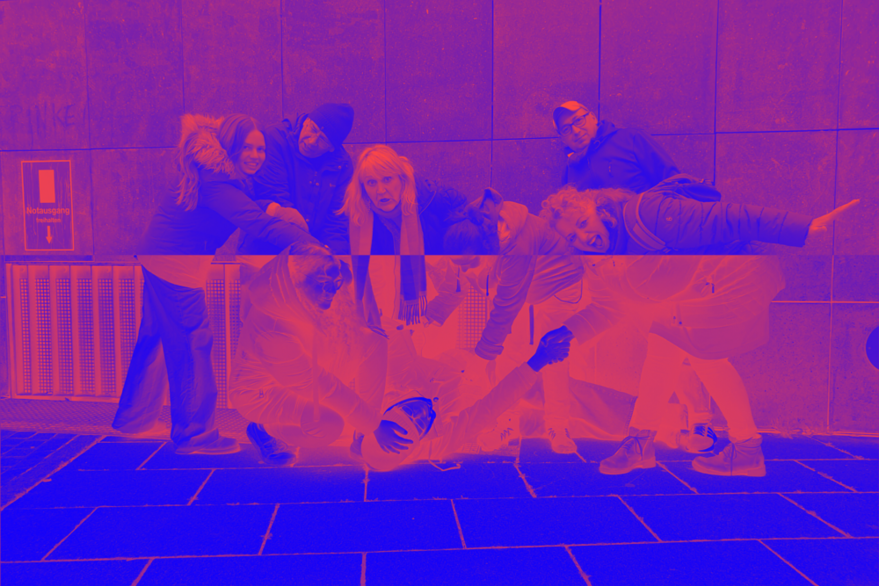 Ein horizontal halbiertes Bild. Die untere Hälfte ist negativ, das gesamte Bild ist von einem Pink-Blau-Filter überzogen. Es ist ein Gruppenfoto der Schauspieler*innen des Volks*Theaters. Ihre Körperhaltung und Mimik ist geschockt, panisch und chaotisch.