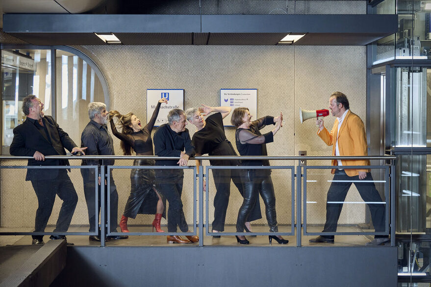 7 Personen in einer theatralischen Szene mit Megaphon in einer U-Bahnhaltestelle