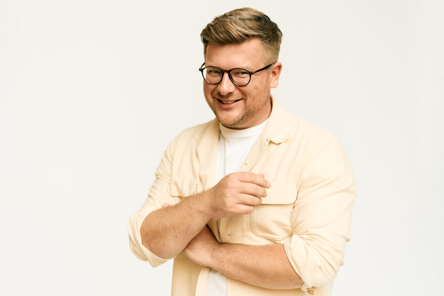Philipp Fleiter in einem cremefarbenen Hemd vor einer weißen Wand.