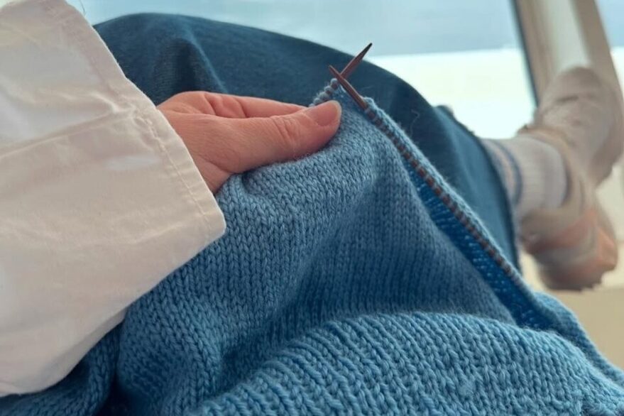 Selbstgestrickter Pullover in blauer Wolle auf Stricknadeln