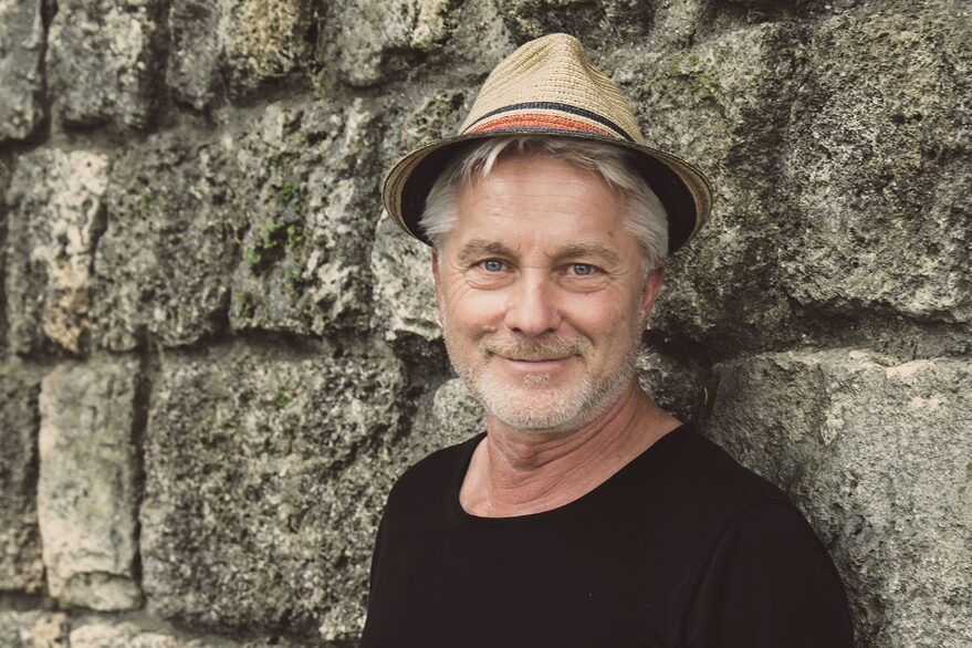 Werner Schmidbauer mit Hutvor einer Steinmauer.