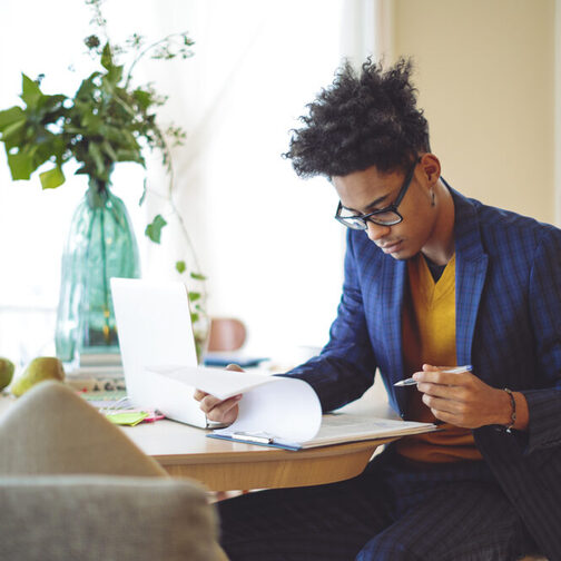 Young man in a blue suit works on documents at a table.