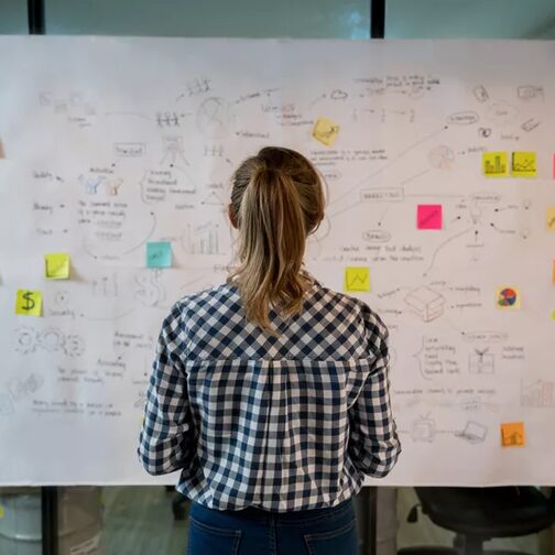 Eine Frau steht vor einem Whiteboard mit Post-its.