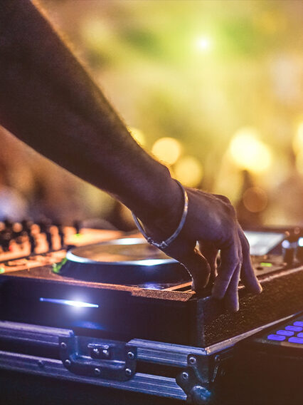 Ein DJ legt mit Mischpult und CD-Player vor Publikum auf.