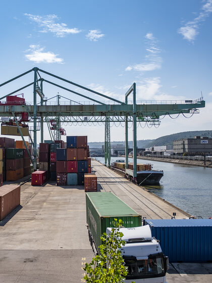 Blick auf ein Hafengelände am Flussufer mit vielen bunten Containern und einem großen Kran.