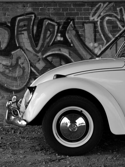 Ein schwarz-weiß Bild mit einem VW-Käfer, der vor einer Graffity-Wand steht.