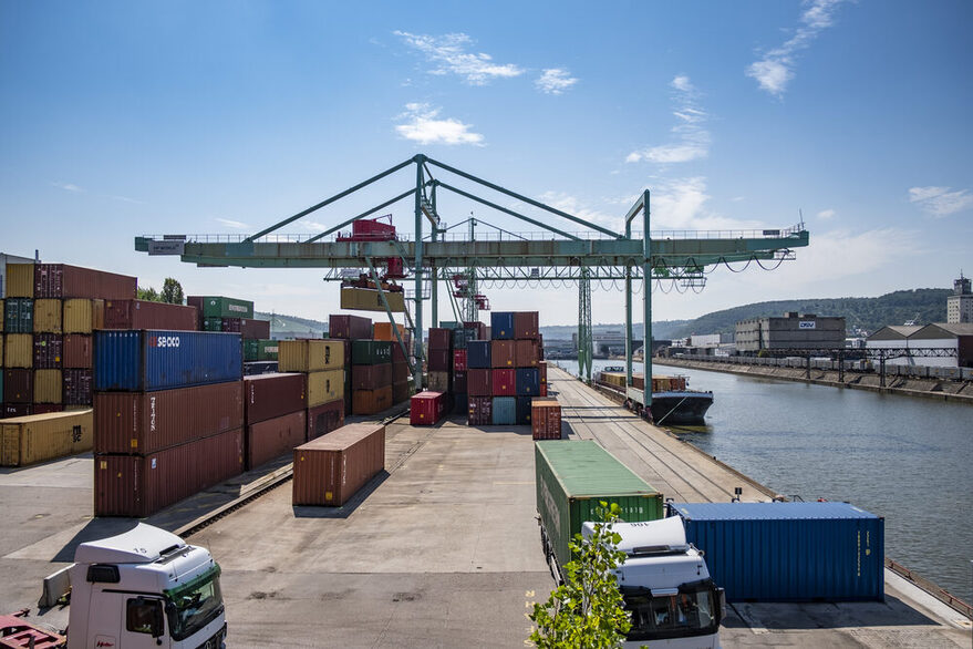 View of a port area on the riverbank with many colorful containers and a large crane.